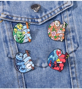 Detail of four cartoon sloth enamel pins showing camping and beach scenes on denim jacket