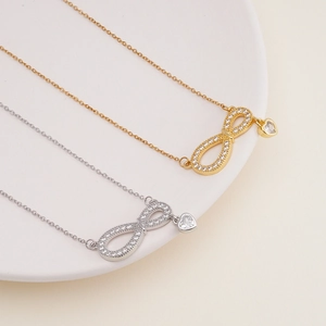 Gold and silver infinity heart necklaces with cubic zirconia on white ceramic tray