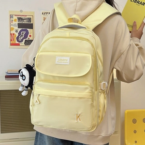 Dettaglio dello zaino in nylon giallo chiaro con tasche a zip e grazioso ciondolo cartone