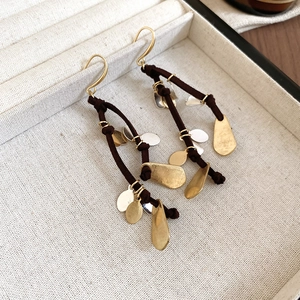 Close-up of teardrop tassel earrings with metallic charms in a beige linen jewelry box