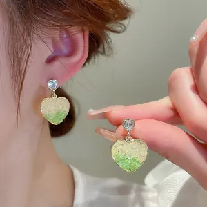 Macro detail of heart earrings with yellow-green gradient crystals and silver plating