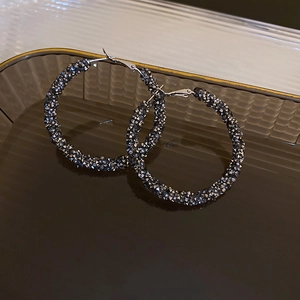 Close-up of geometric gunmetal hoop earrings with micro-inlaid rhinestones on a glass tray