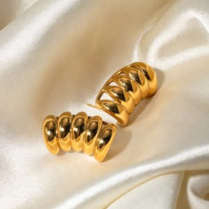 Makroaufnahme goldener gerippter Kokon-Ohrringe auf beigem Satin-Hintergrund
