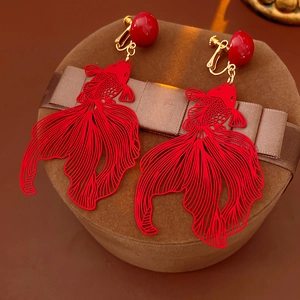 Détail des boucles d'oreilles clips poisson rouge évidées sur une boîte à bijoux en velours brun