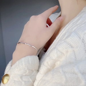 Detail of minimalist S925 sterling silver wavy bangle on a woman's wrist with knit sweater