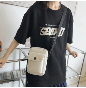 Close-up of off-white canvas messenger bag with black strap and front flap pocket detail