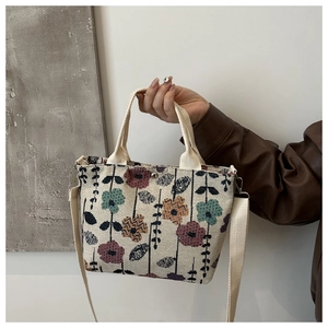 Floral knit tote bag shown held by hand with long shoulder strap detail