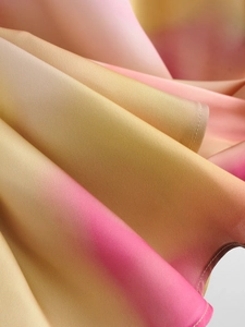 Detailed close-up of glossy satin tie-dye fabric showing soft pink and yellow gradient texture