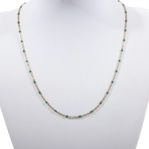 Detail of a thin gold beaded necklace with vibrant green enamel beads on a jewelry bust