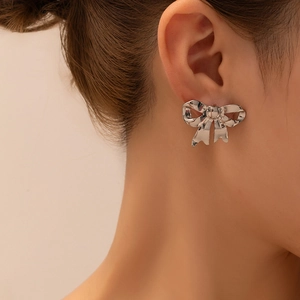 Detailed close-up of a silver bow-shaped stud earring worn on a model's ear lobe
