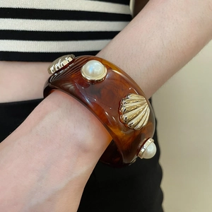 Dettaglio del bracciale largo in resina ambrata con conchiglia dorata e perle