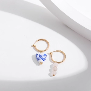 Detail of asymmetric gold earrings with blue floral heart porcelain and pink beads