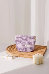 Close-up of purple plush makeup bag with heart patterns and gold zipper on wooden tray