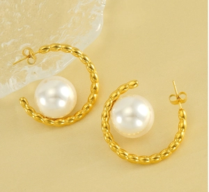 Close-up of C-shaped gold pearl earrings on soft textured fabric background