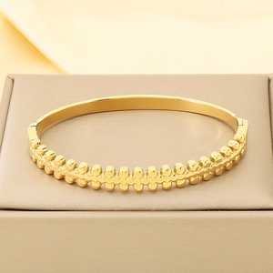 Detail of gold knot bangle with embossed cross patterns on a warm fabric display