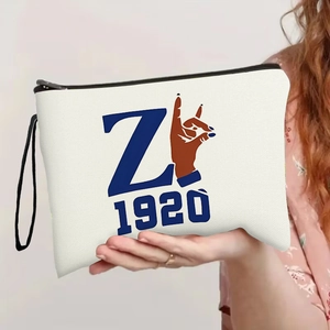 White canvas cosmetic bag with blue 'Z' print, black zipper and handle held by hand