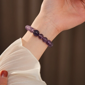 Detail eines Amethyst-Perlenarmbands am Handgelenk mit elegantem Seidenärmel und sanftem Licht