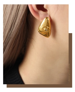 Detail of gold geometric evil eye earrings with zircon inlay worn by a model