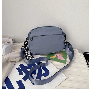 Détail du sac bandoulière en nylon bleu avec étiquette mode et breloque ours damier