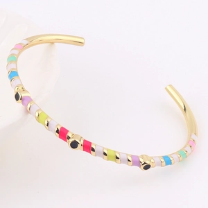 Detail of thin gold bracelet with colorful enamel stripes and black eye-shaped dots