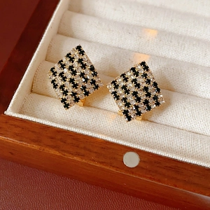 Détail de boucles d'oreilles losanges avec motif à damier noir et blanc en boîte de velours