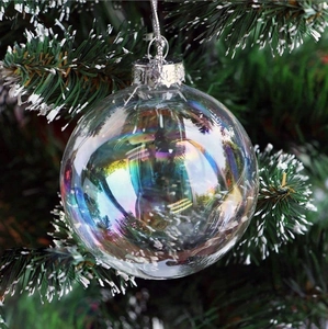 Iridescent transparent Christmas ball ornament hanging on a green festive tree branch