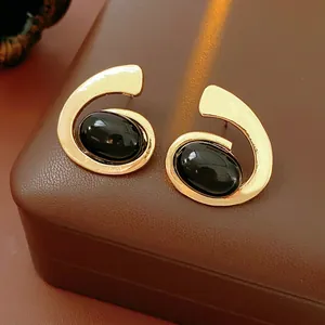 Minimalist spiral gold earrings with oval black stones on a leather background