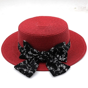 Detail view of red flat-top straw sun hat featuring elegant black floral ribbon bow