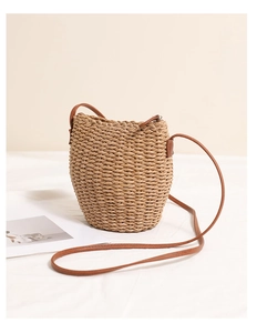 Detail of a cylindrical straw bucket bag with brown leather strap and top zipper closure