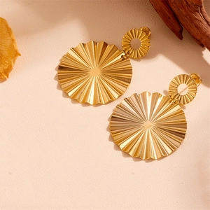 Detail of gold fan-shaped pleated stainless steel earrings on a textured background