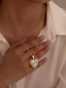 Close-up of golden heart locket necklace with colorful abalone shell on a model