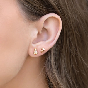 Close-up of asymmetrical gold earrings featuring heart zircon and dark crown skull design