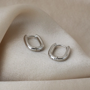 Détail des boucles d'oreilles créoles argentées en U sur fond de soie douce