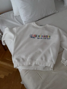 White crewneck sweatshirt with colorful letter embroidery on a clean minimalist background