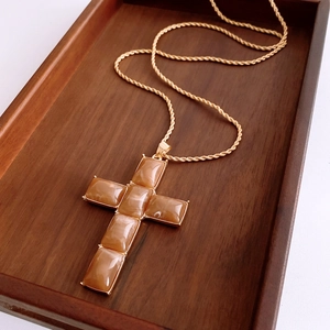 Macro shot of gold cross necklace with amber resin inlays on a dark wooden tray