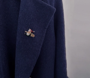 Detail of Christmas snowflake brooch with red hat and pearls on a navy wool coat