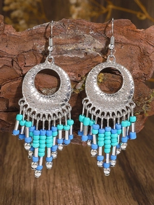 Close-up of bohemian silver drop earrings with blue and green beads on tree bark