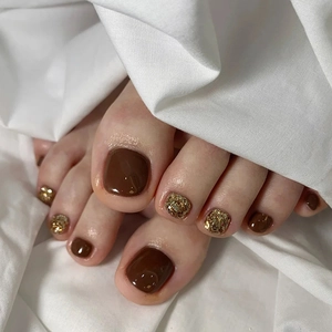 Close-up of deep brown and gold glitter press-on toenails on soft white fabric