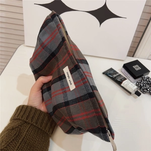 Detail of red plaid canvas cosmetic bag with metal zipper and brand label shown in hand