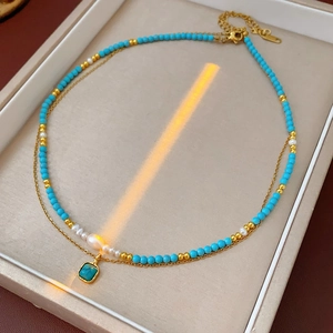 Dettaglio di una collana a doppio strato placcata oro con perle turchesi e pendente quadrato