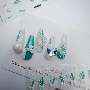 Detail of green handmade press-on nails featuring 3D lilies, pearls, and a large blue butterfly