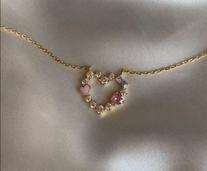 Dettaglio macro di una collana placcata oro 14k con smalto a cuore rosa e gemme colorate