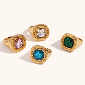 Set of four 18K gold plated rings with colorful square cut gemstones on a beige surface
