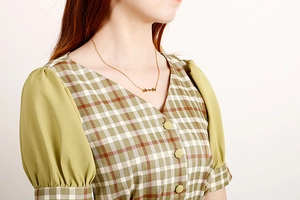 Close-up of minimalist gold necklace with butterfly charms on a model in V-neck dress