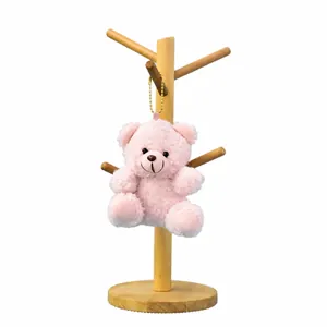 Cute pink teddy bear plush keychain hanging on a minimalist wooden display stand