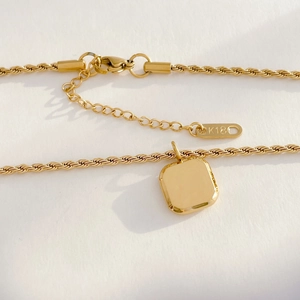 Detailed close-up of K18 engraved metal tag on golden twisted rope chain necklace