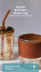 Detail of amber glass cup with bamboo texture, brown leather sleeve and glass straw