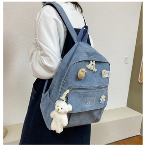 Detalle de mochila de pana azul claro con insignias de osos y colgante de oso de peluche