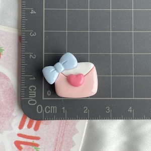 Detailed scale view of a pink resin envelope charm with blue bow for DIY crafts
