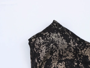 Detail of elegant black dress showing metallic gold foil texture on one-shoulder neckline